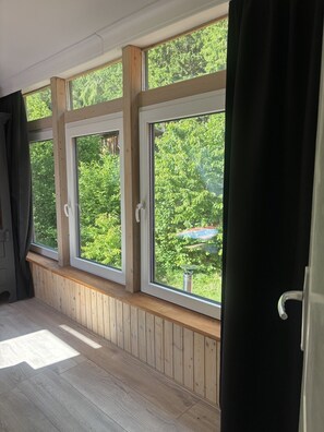 A room with three large windows, wooden paneled walls, and a view of greenery outside. - BergwaldHaus Willingen, Diemelsee, Winterberg (Brilon)