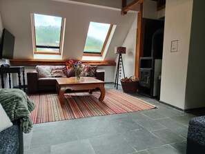 A cozy living room with a sofa, a wooden coffee table, a fireplace, and a large window. - BergwaldHaus Willingen, Diemelsee, Winterberg (Brilon)