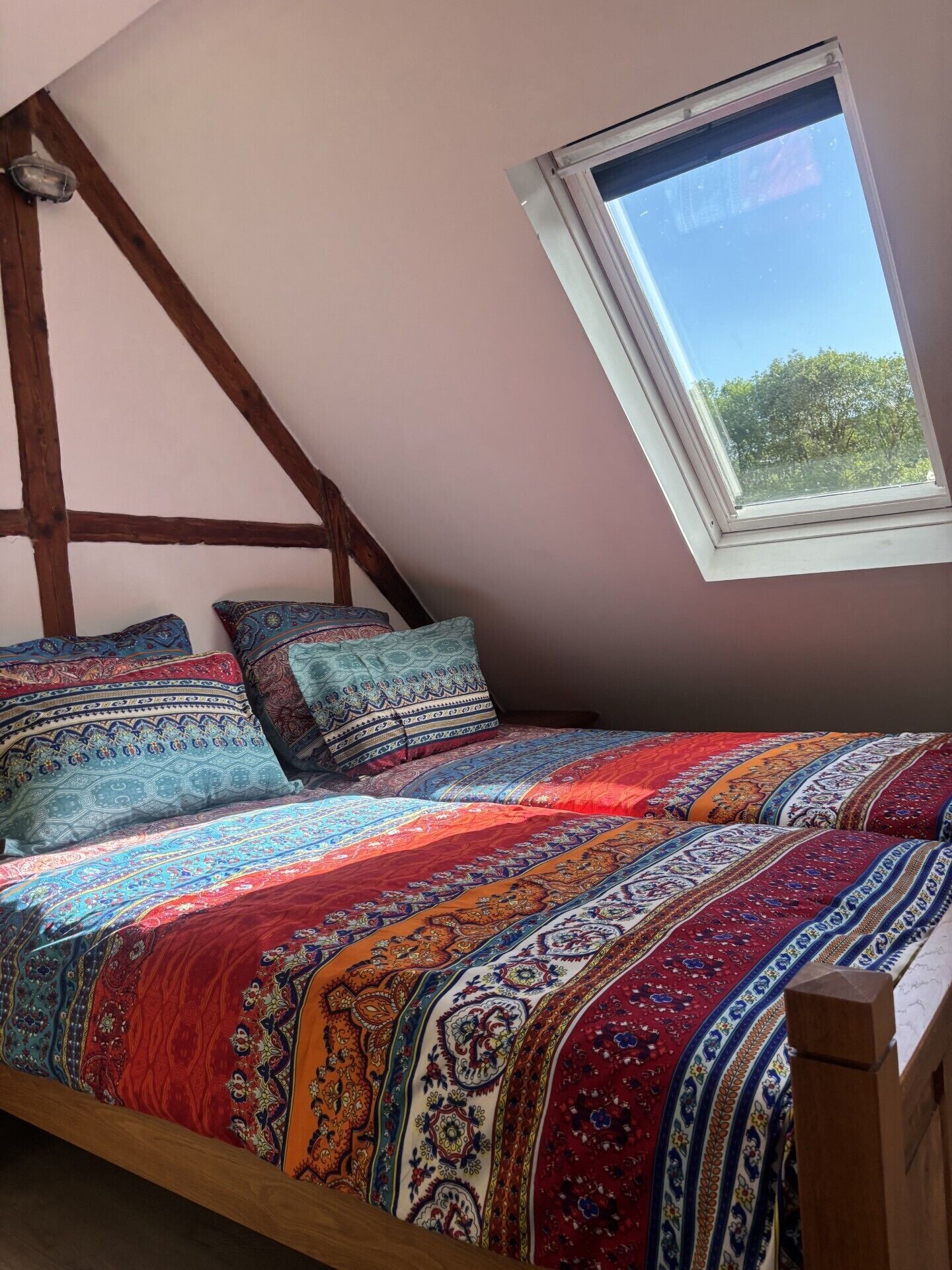 Quarto com teto inclinado, claraboia, estrutura de cama de madeira e colcha colorida.
