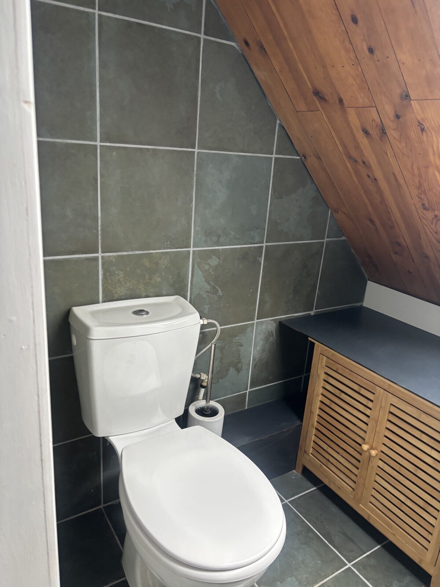 A bathroom with a white toilet, a wooden cabinet, and a tiled wall.