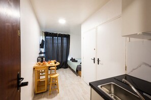 Uma cozinha compacta com mesa, cadeiras, pia e uma cama ao fundo.