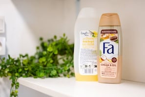 Deux bouteilles de crème de douche sont posées sur une étagère, avec une plante verte en arrière-plan.