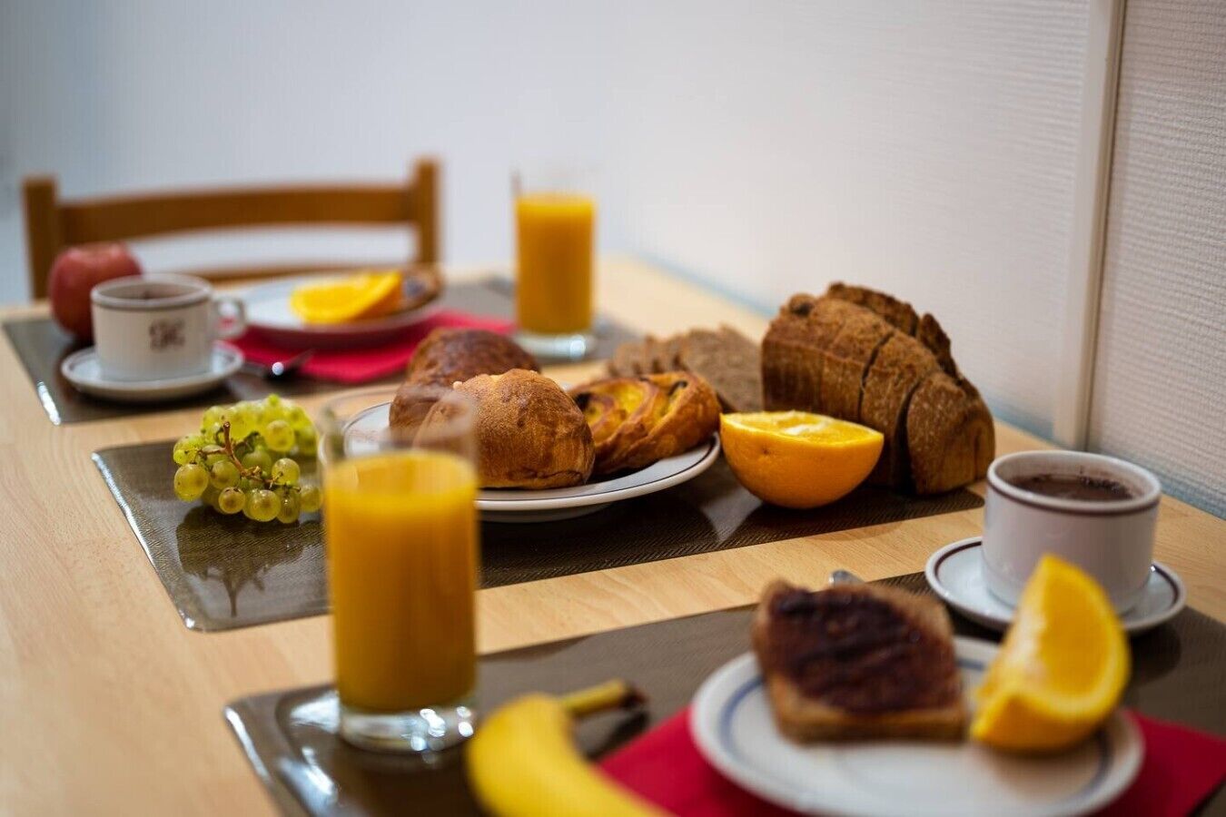 Une table de petit-déjeuner avec du pain, des fruits, un verre de jus d’orange et une tasse de café.