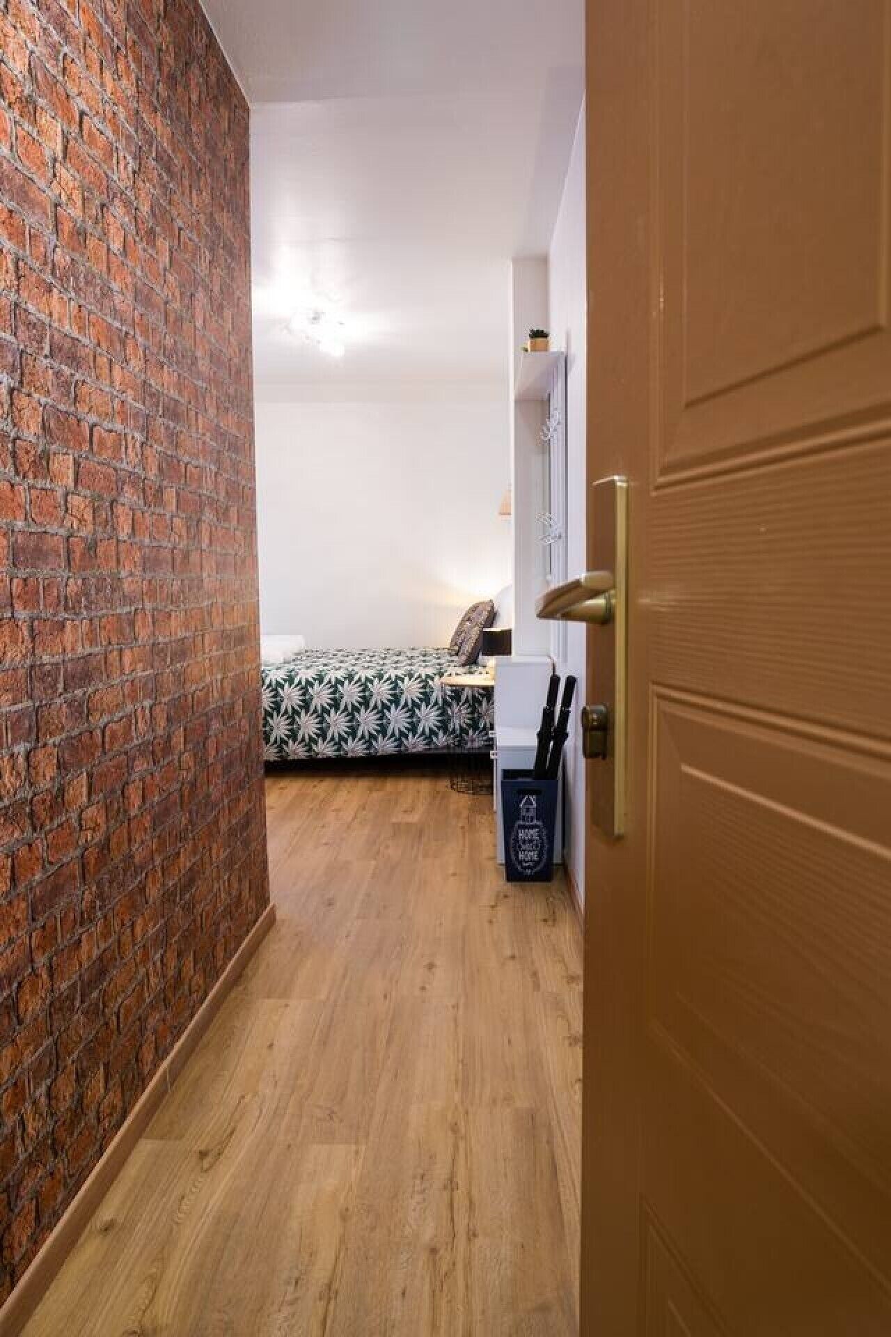 Une pièce avec un mur en briques, un lit recouvert d’une courtepointe à motifs, une petite table et une poubelle.