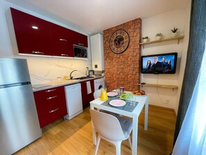 Eine kompakte Küche mit modernen Geräten, ein Essbereich mit Tisch für Zwei und ein an der Wand montierter Fernseher.