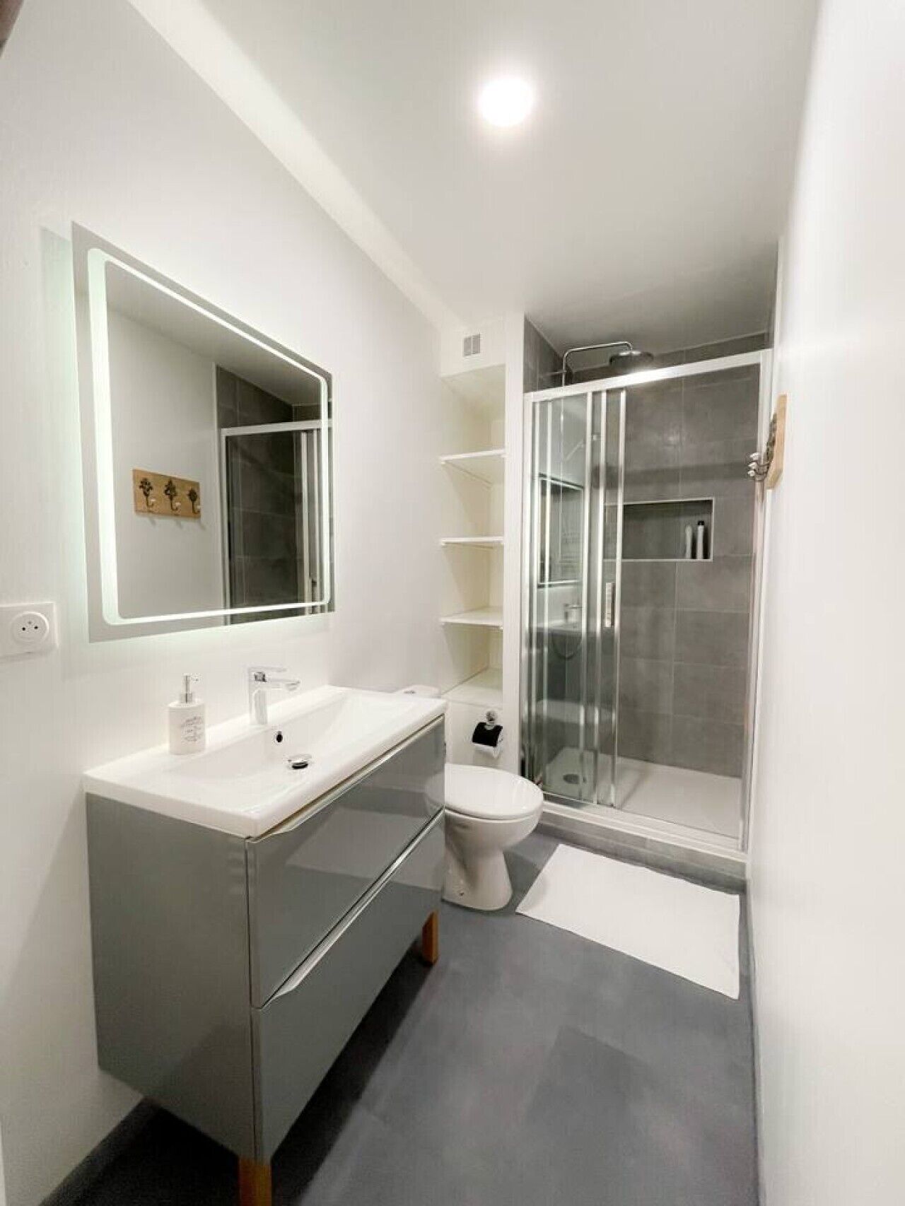 A modern bathroom with a large mirror, a white sink, a toilet, and a glass-enclosed shower.
