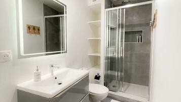 A modern bathroom with a large mirror, a white sink, a toilet, and a glass-enclosed shower.