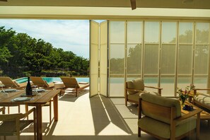 Ein moderner Essbereich im Freien mit Blick auf einen Pool, Holzmöbel und einer Schiebeglas-Tür.