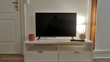 A white entertainment unit with a flat-screen TV, a red mug, a clock, and a keyboard.