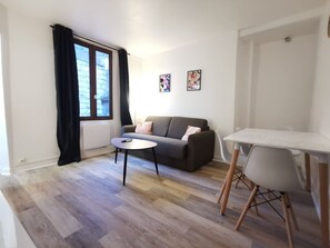 Un saló amb un sofà, una taula rodona petita, una taula de dinar i una finestra amb cortines.