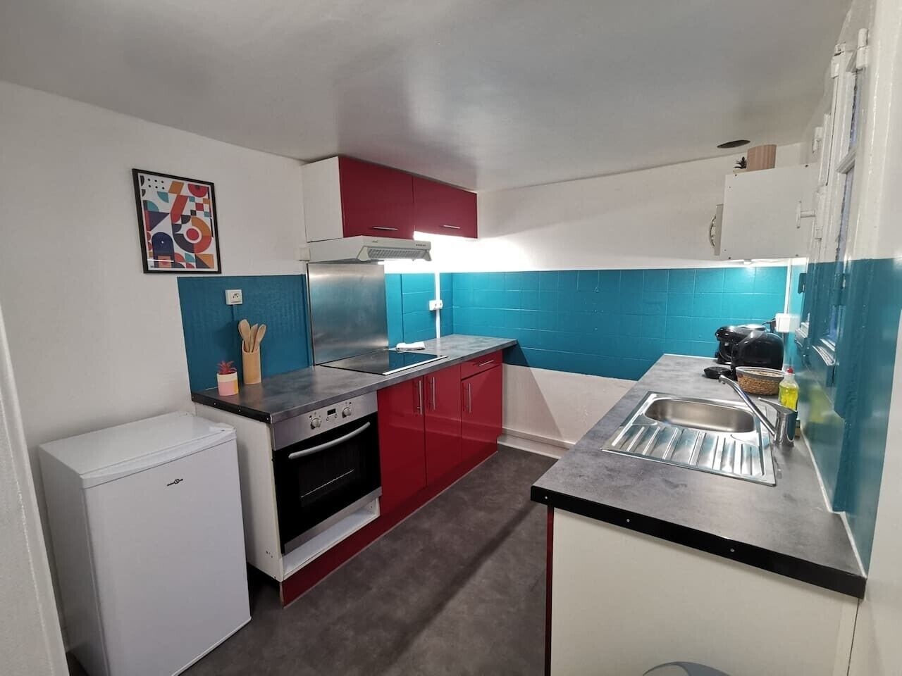 A compact kitchen with a refrigerator, stove, sink, and red cabinets.
