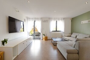 Ein modernes Wohnzimmer mit einem Flachbildfernseher, einer Couch, einem Couchtisch und einer Glastür, die zu einem Außenbereich führt.