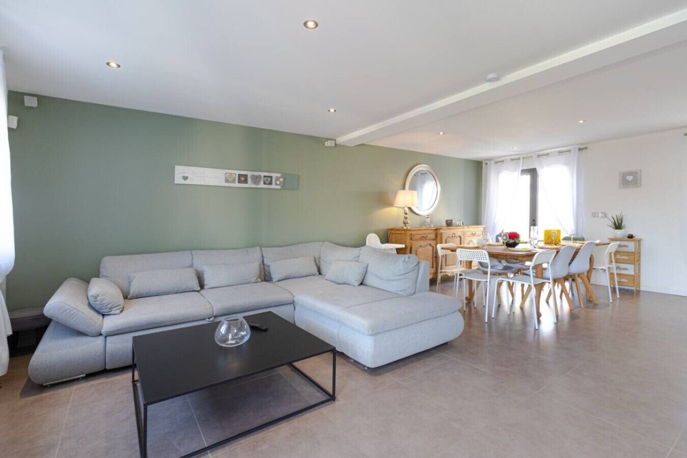 Ein Wohnzimmer mit Ecksofa, ein Essbereich mit Tisch und Stühlen sowie eine Küche mit Arbeitsplatte und Schränken.