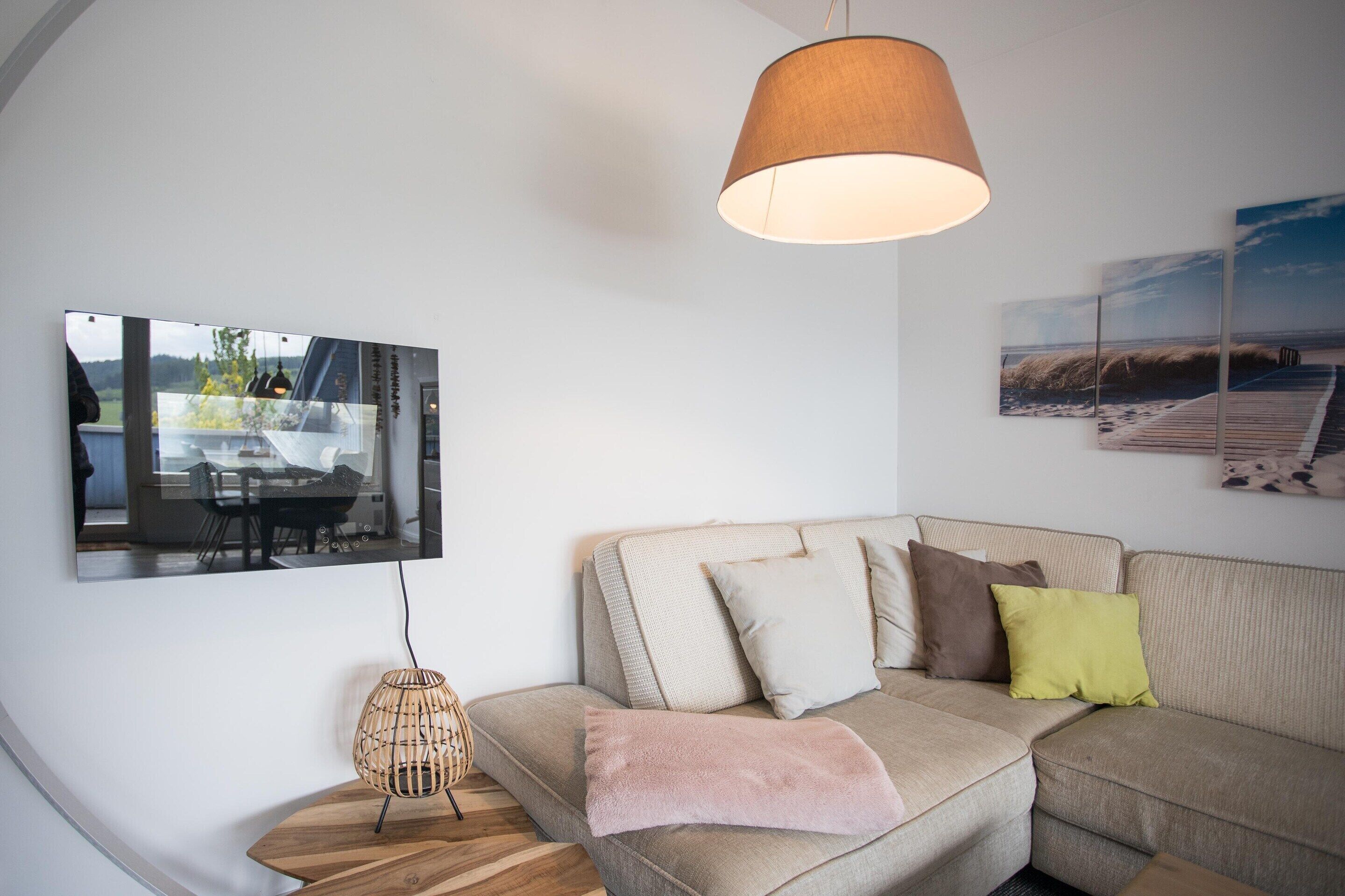 A modern living room with a sofa, cushions, a hanging light fixture, and artwork on the walls.