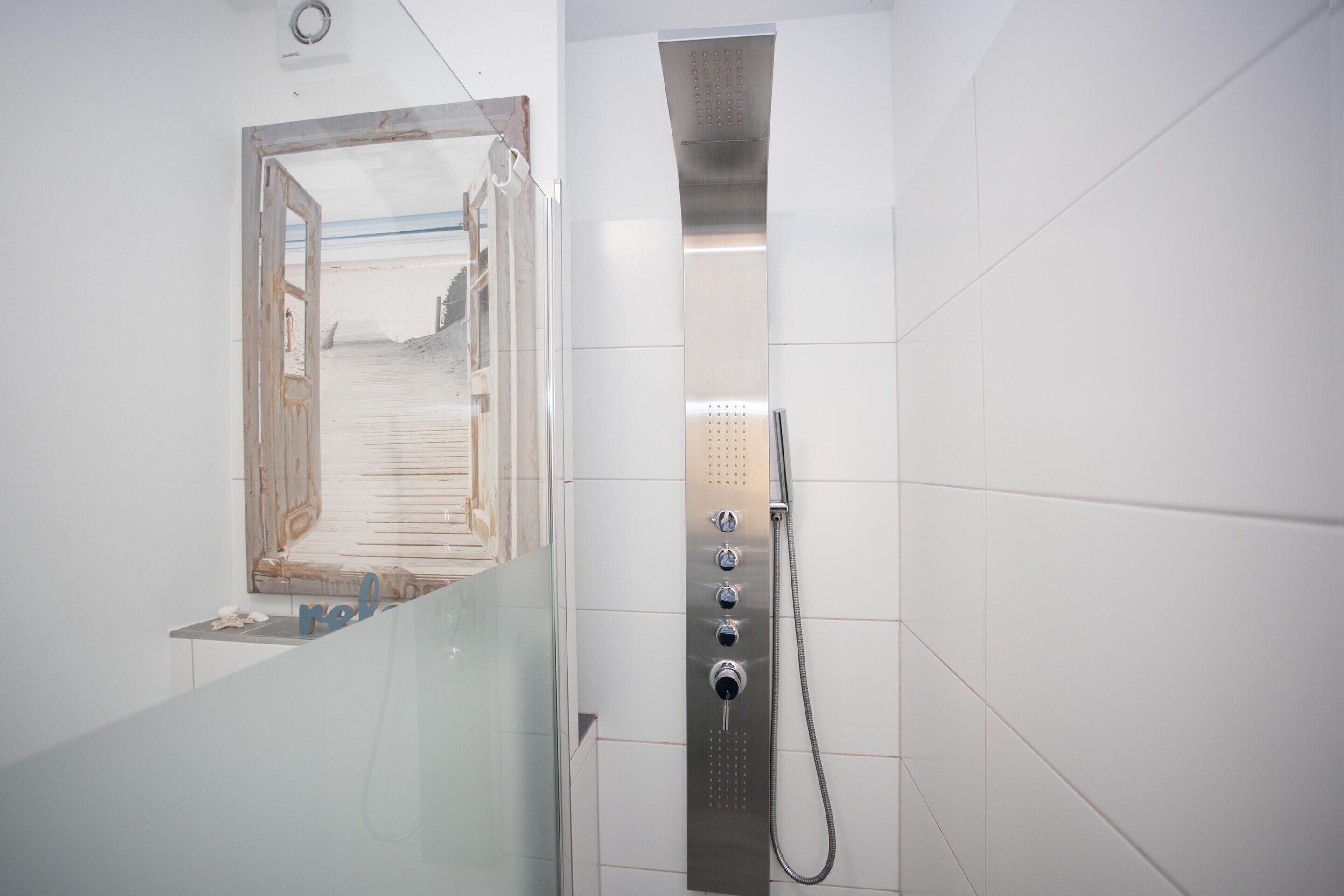 A bathroom with a shower stall, a glass door leading to a beach view, and a towel rack.