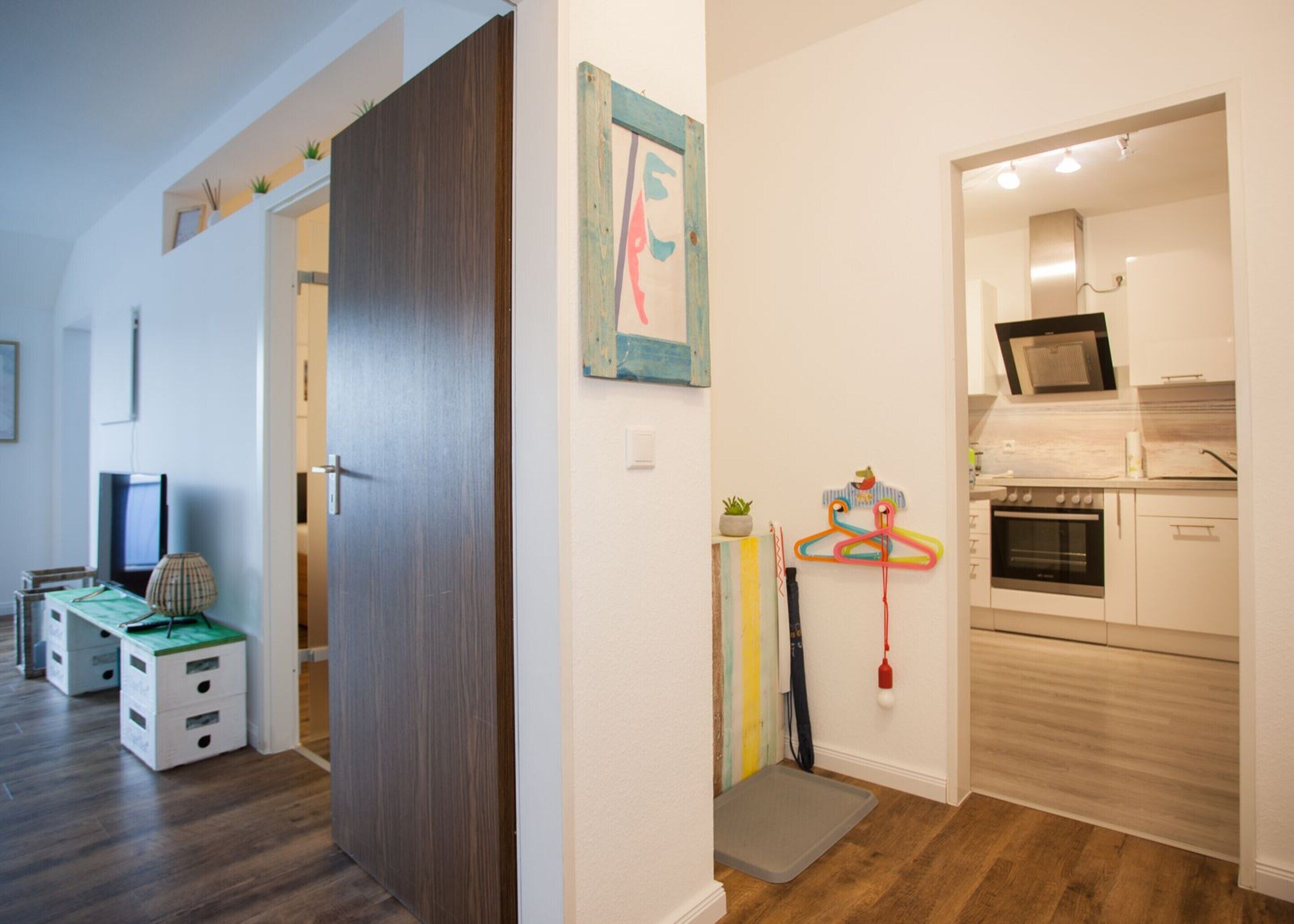 Un espacio habitable compacto con kitchenette, televisor y una puerta que da a otra habitación.