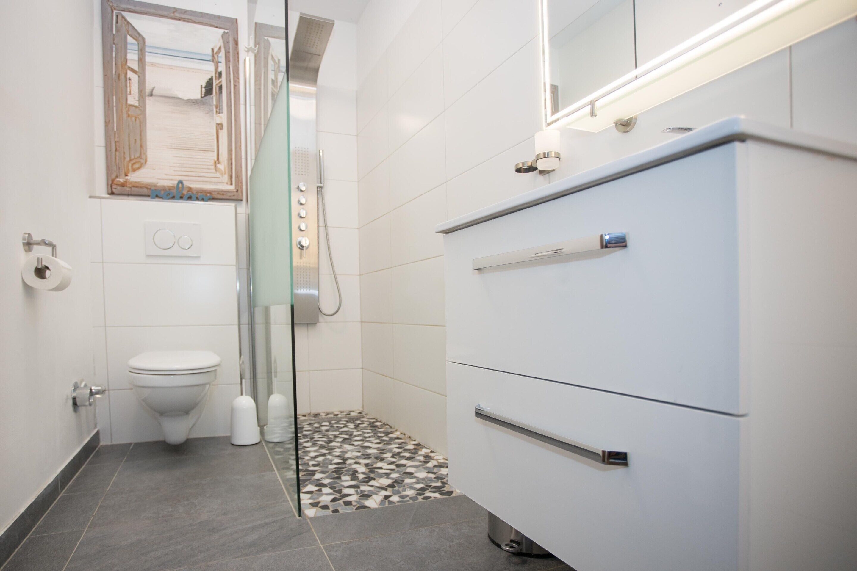 A bathroom with a toilet, a shower, and a vanity with a mirror.