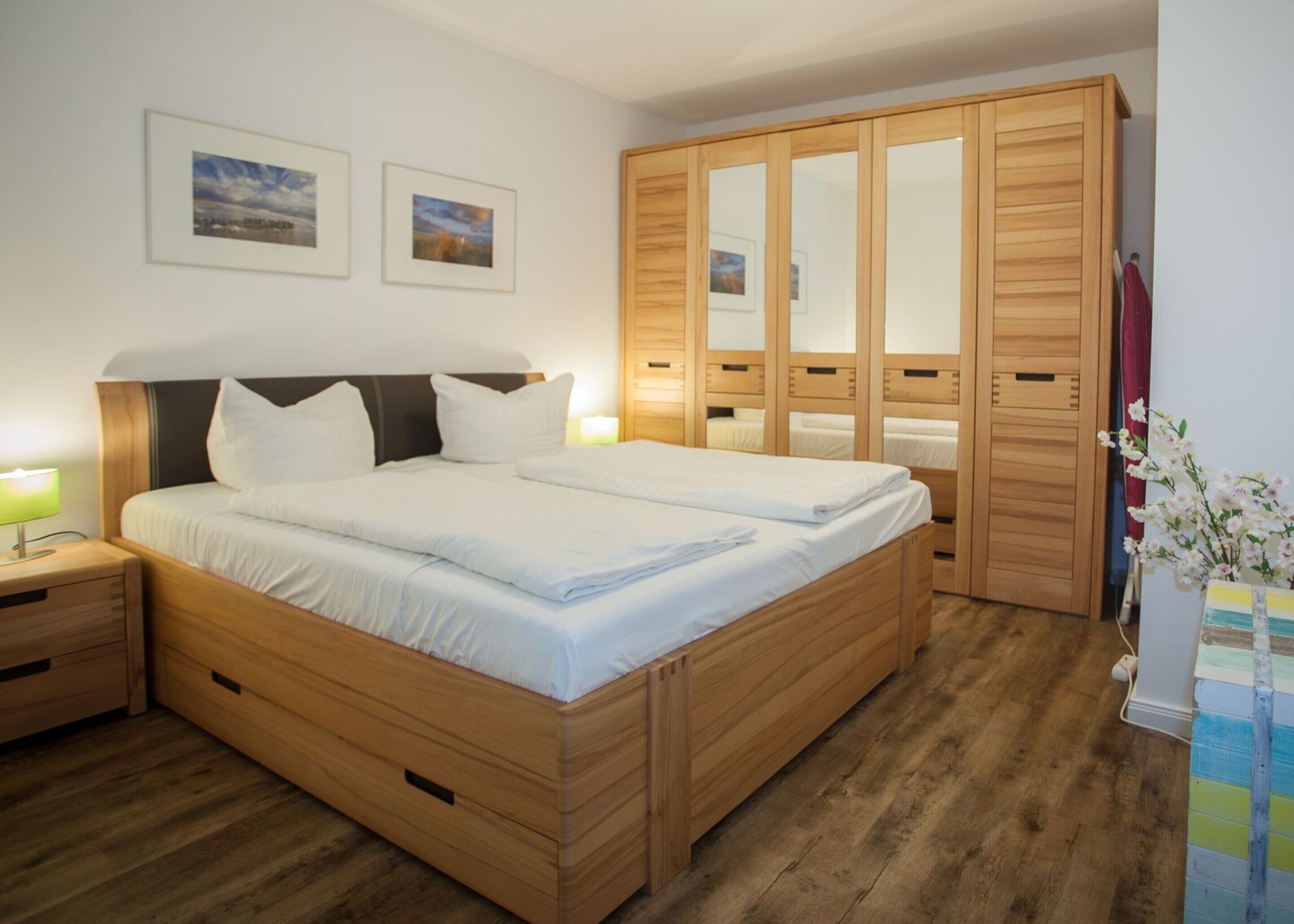 Un dormitorio con una cama de madera, dos mesitas de noche, un armario y dos cuadros enmarcados en la pared.
