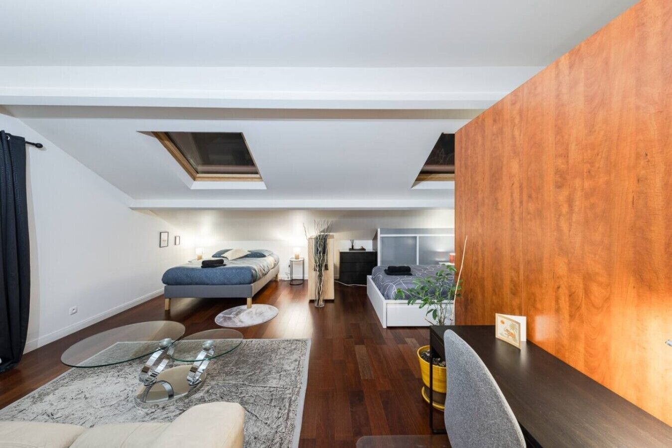Une chambre de style loft moderne, dotée de fenêtres de toit, d’un lit, d’un bureau et d’un coin salon.