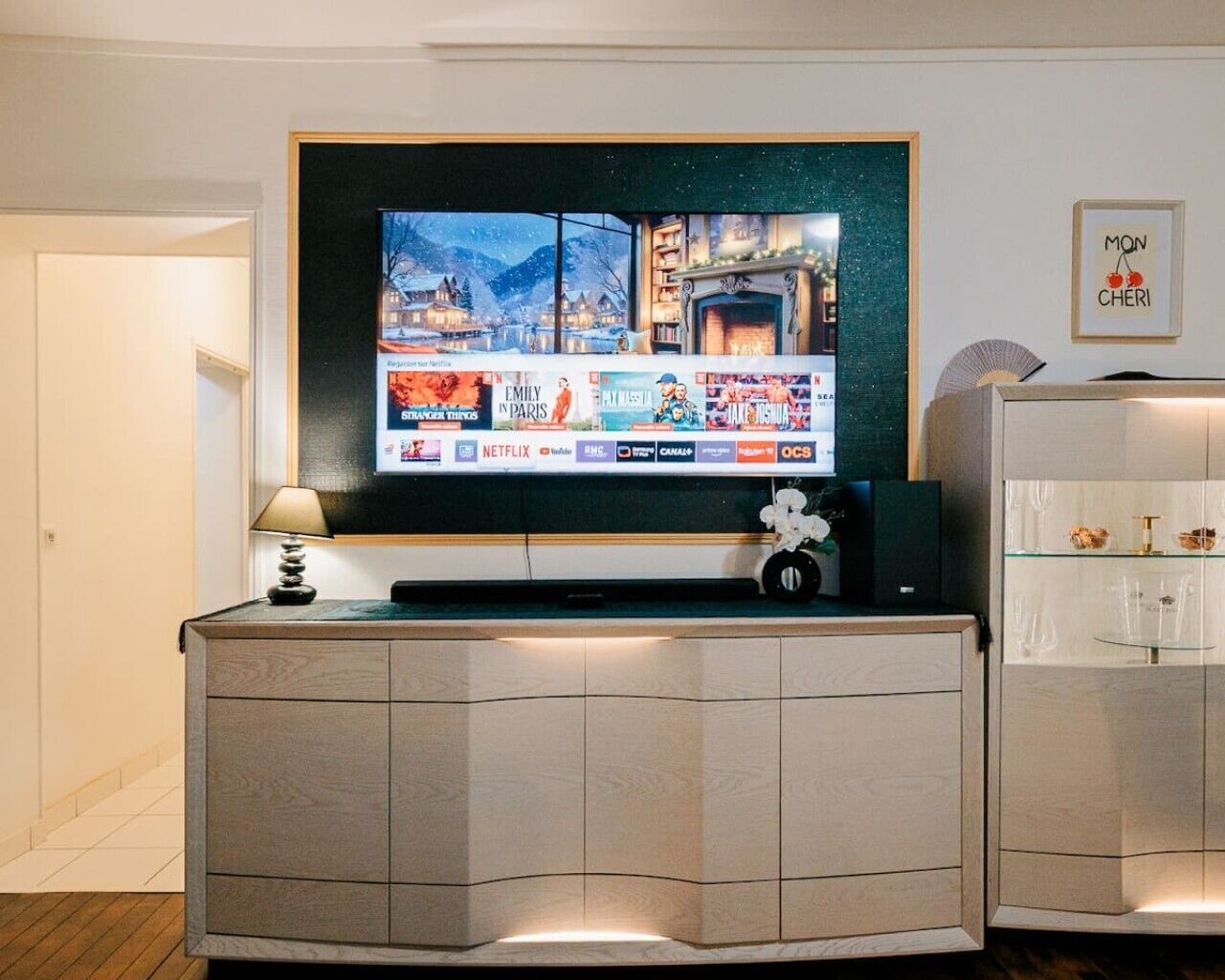 Un salon moderne avec un téléviseur à écran plat fixé sur un meuble en bois, une petite table avec une lampe et un objet décoratif posé sur le meuble.