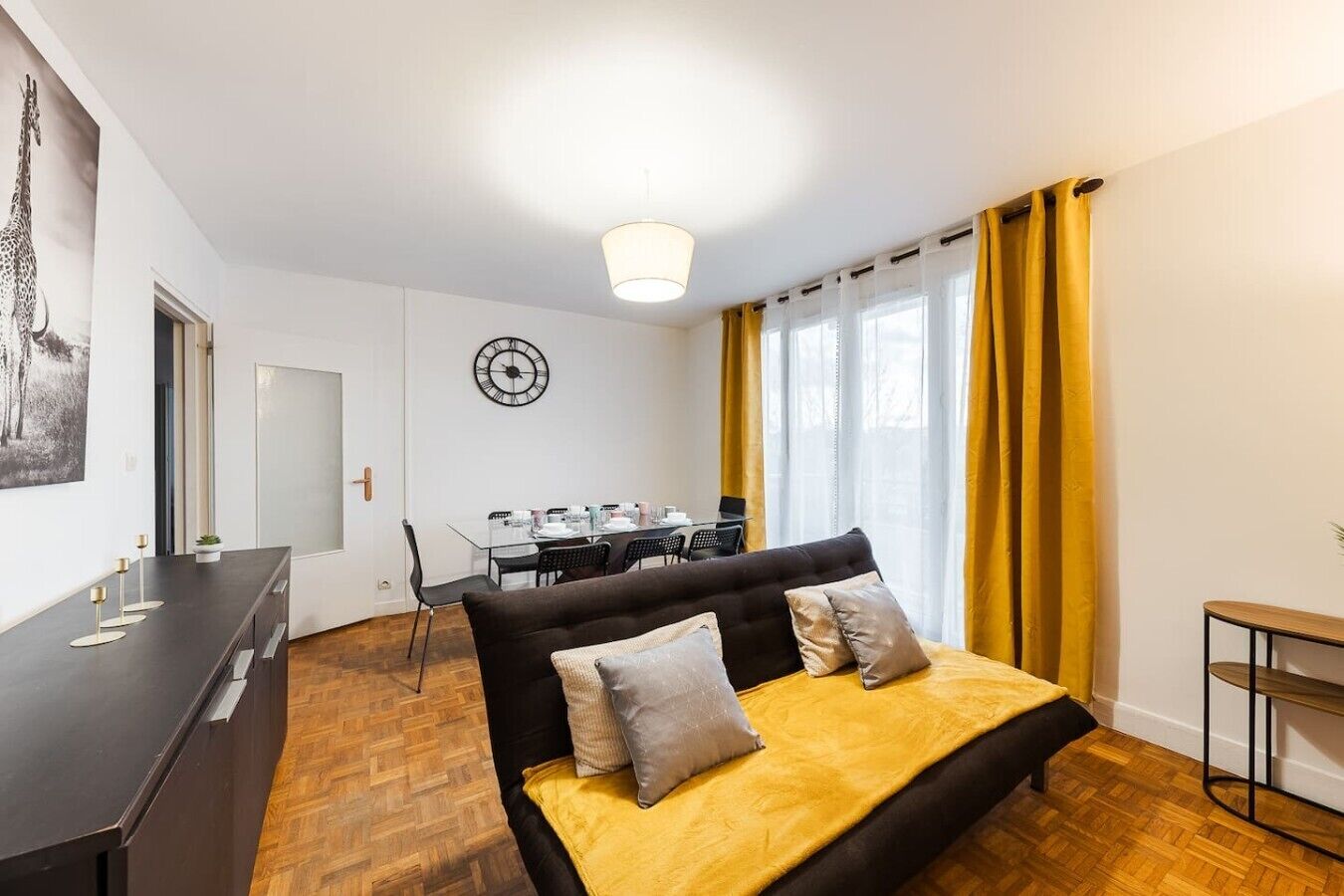 Ein Schlafzimmer mit Bett, Schreibtisch, Stuhl, Esstisch und einer Wanduhr.
