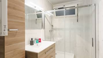 Ein modernes Badezimmer mit einem Holzlager, einer Duschkabine aus Glas und einem weiß gefliesten Boden.