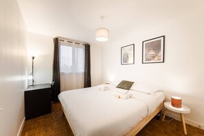 Une chambre d’hôtel avec un lit, une table de chevet, une lampe, une fenêtre avec des rideaux et deux tableaux encadrés accrochés au mur.