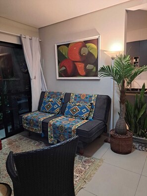 A living room with a sofa, a dining table, a potted plant, and a painting on the wall. - GREAT APARTMENT IN NORTH ENGLISH BEACH (Ingleses do Rio Vermelho)