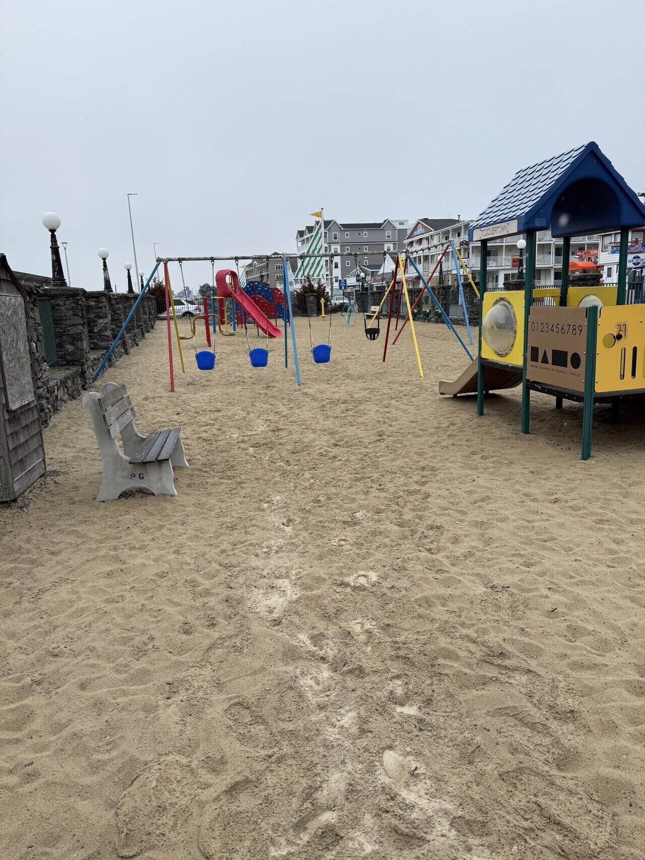 Un’area giochi sulla spiaggia con altalene, scivoli e una zona ombreggiata.