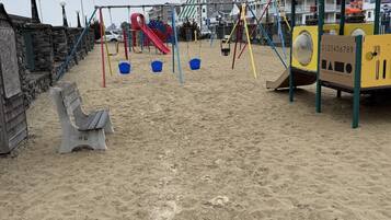 Un’area giochi sulla spiaggia con altalene, scivoli e una zona ombreggiata.