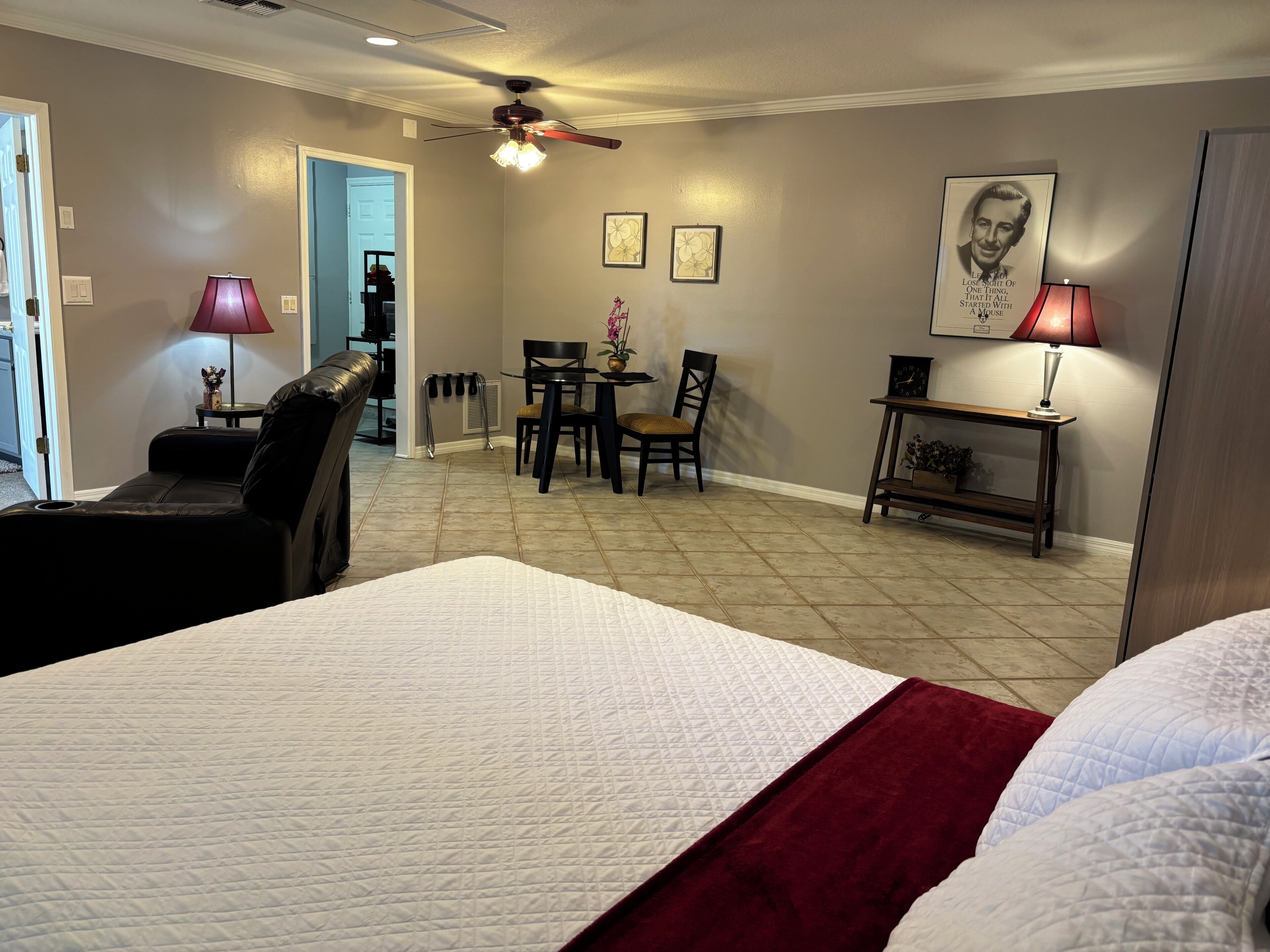 Quarto de hotel com cama, escrivaninha, cadeira, mesa e ventoinha no teto.