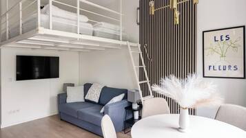 A modern living room with a bunk bed, a sofa, a dining table, and a wall-mounted TV.