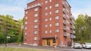 Monikerroksinen rakennus, jossa on punainen julkisivu, parvekkeita ja sisäänkäynti katutasossa.