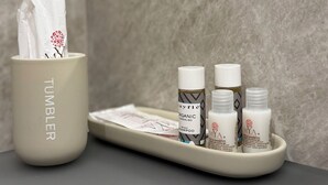 Ein Badezimmer-Waschtisch mit Taschentuchhalter, einer Ablage mit drei Shampoo-Flaschen und einem Spiegel.