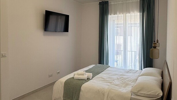 Ein Schlafzimmer mit einem Bett, einem an der Wand montierten Fernseher, einem Holztisch und einer Pendelleuchte.