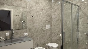 Ein modernes Badezimmer mit Duschkabine aus Glas, einem Bidet, einer Toilette und einem Waschtisch mit Spiegel.