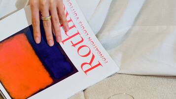 Una persona che tiene in mano una rivista con copertina rossa e blu, un bicchiere di un liquido scuro e un vassoio con una tazza.