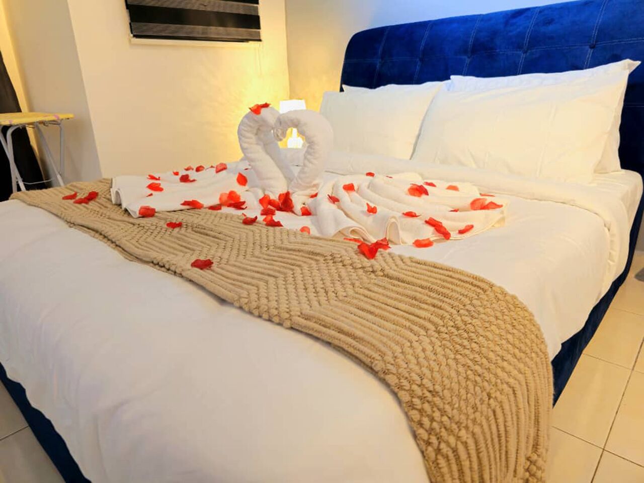 Ein Bett mit Handtüchern in Herzform und Rosenblättern, ein blauer Kopfteil sowie eine beige Decke.