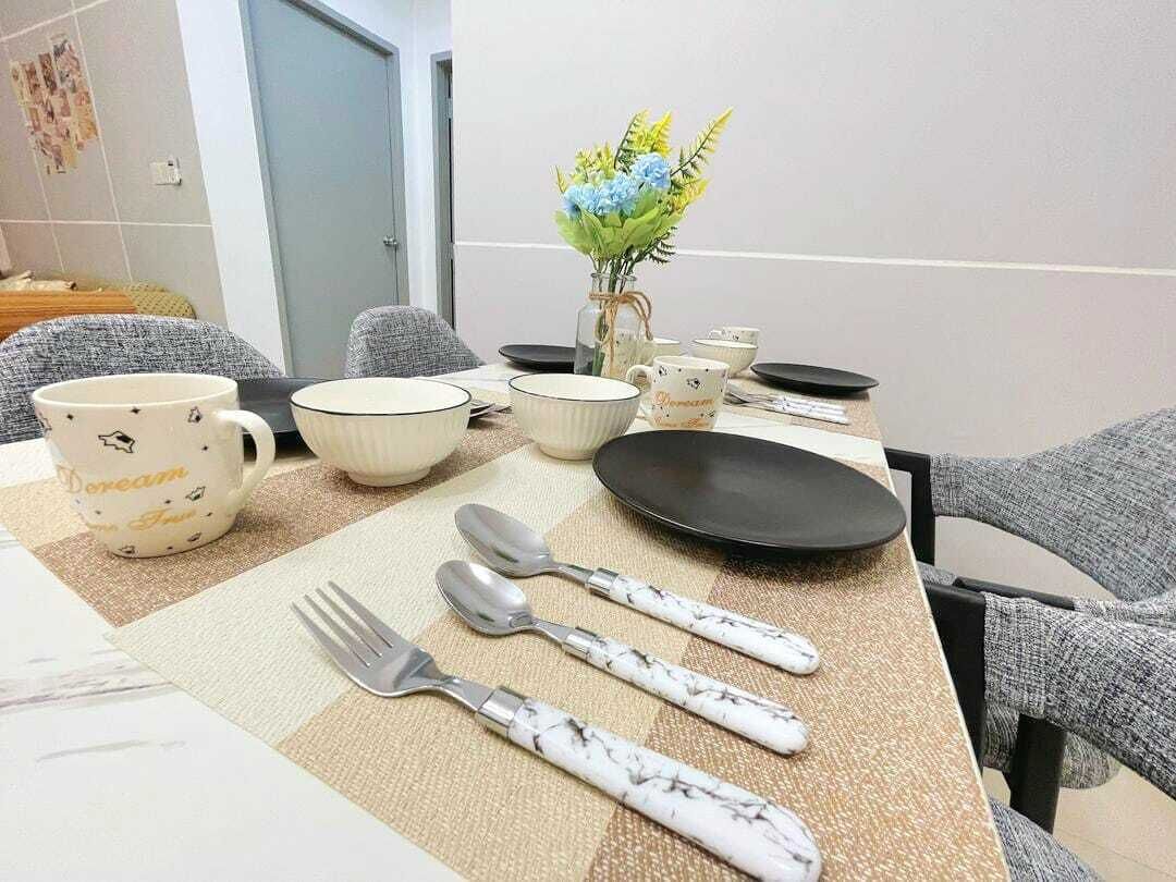 A dining table set with plates, bowls, cups, and cutlery, with a vase of flowers and a wall calendar.