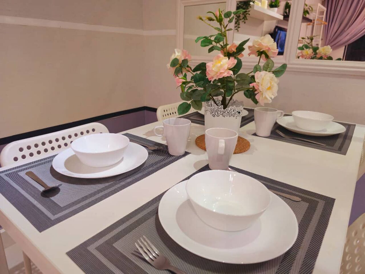 A dining table set with white plates, bowls, and cups, a vase with flowers, and a chair with a white cushion.