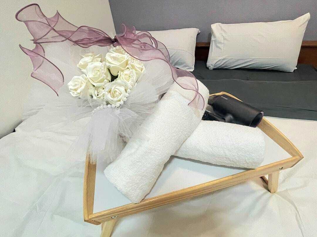 A bed with white linens, a bouquet of white roses, and a wooden tray.