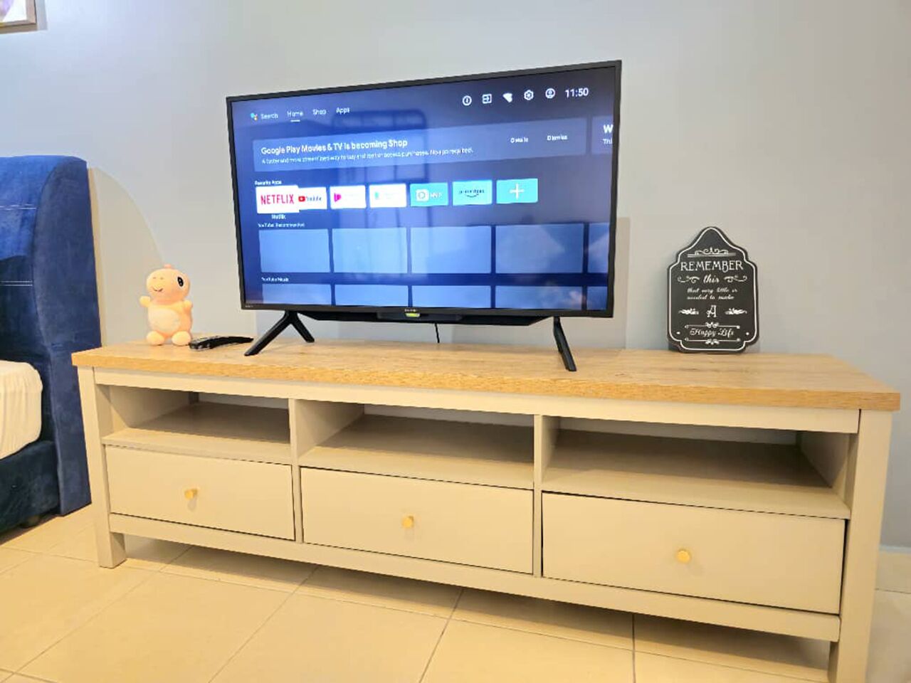 A television on a wooden TV stand with a drawer, a small figurine, and a sign on the wall.