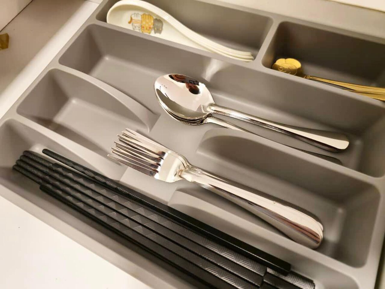 A drawer with compartments containing a spoon, fork, chopsticks, and a knife.