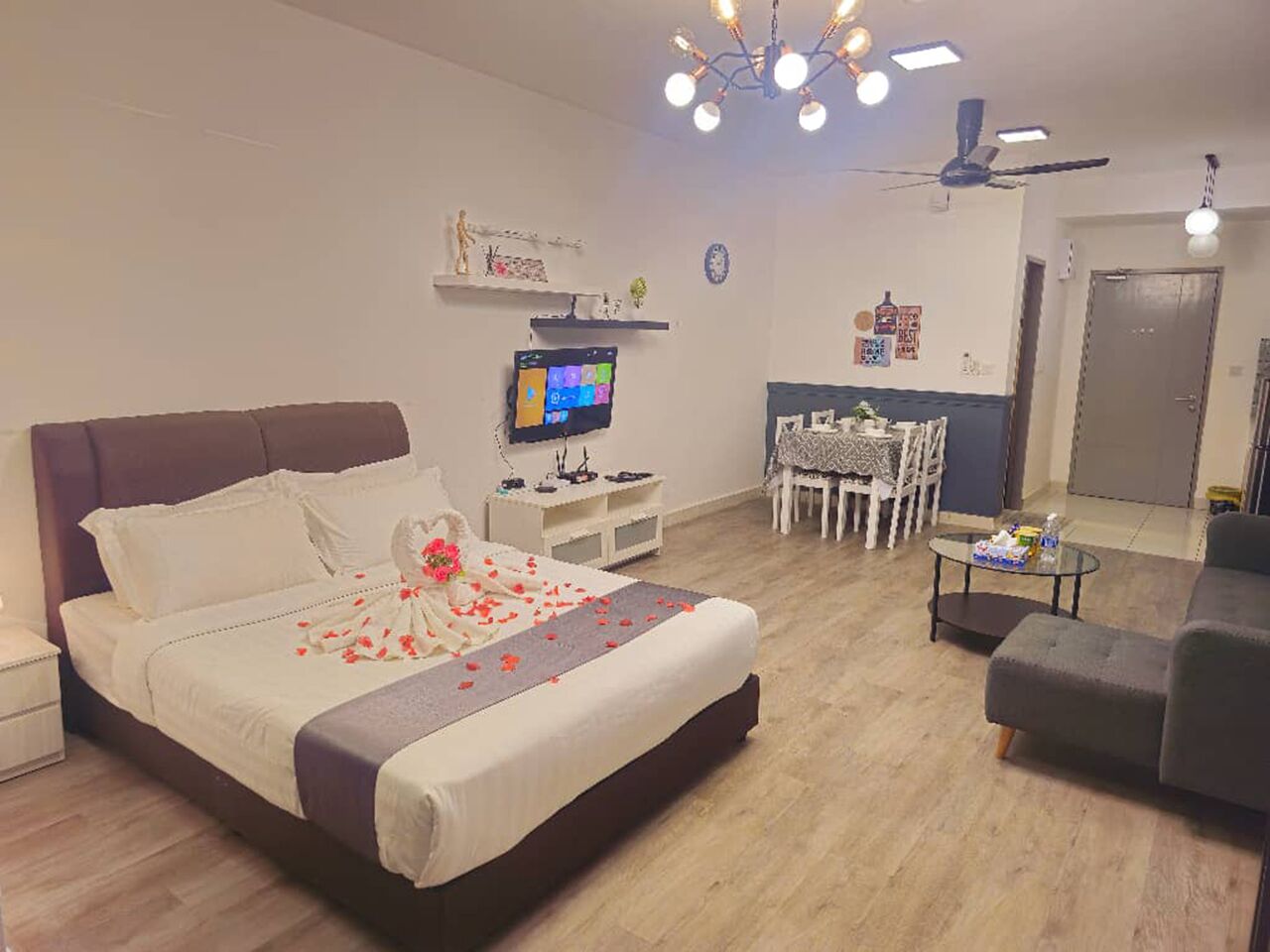 A bedroom with a bed, bedside table, TV, and a dining area with chairs and a table.
