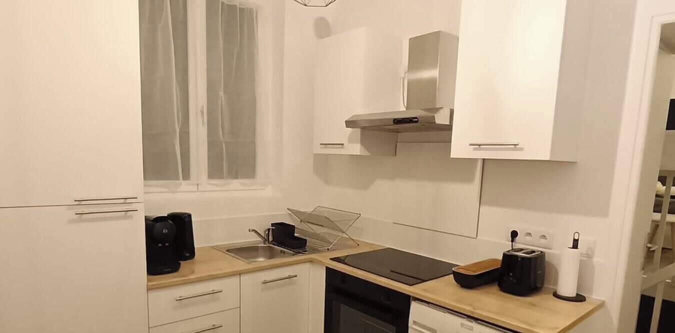 A modern kitchen with white cabinets, a stainless steel range hood, a coffee maker, a toaster, and a dish rack.