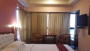 A hotel room with a bed, a table with two chairs, a television, and curtains.