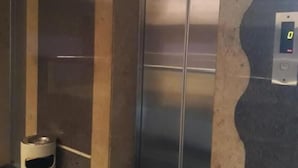 An elevator with a digital display, a trash bin, and a marble floor.