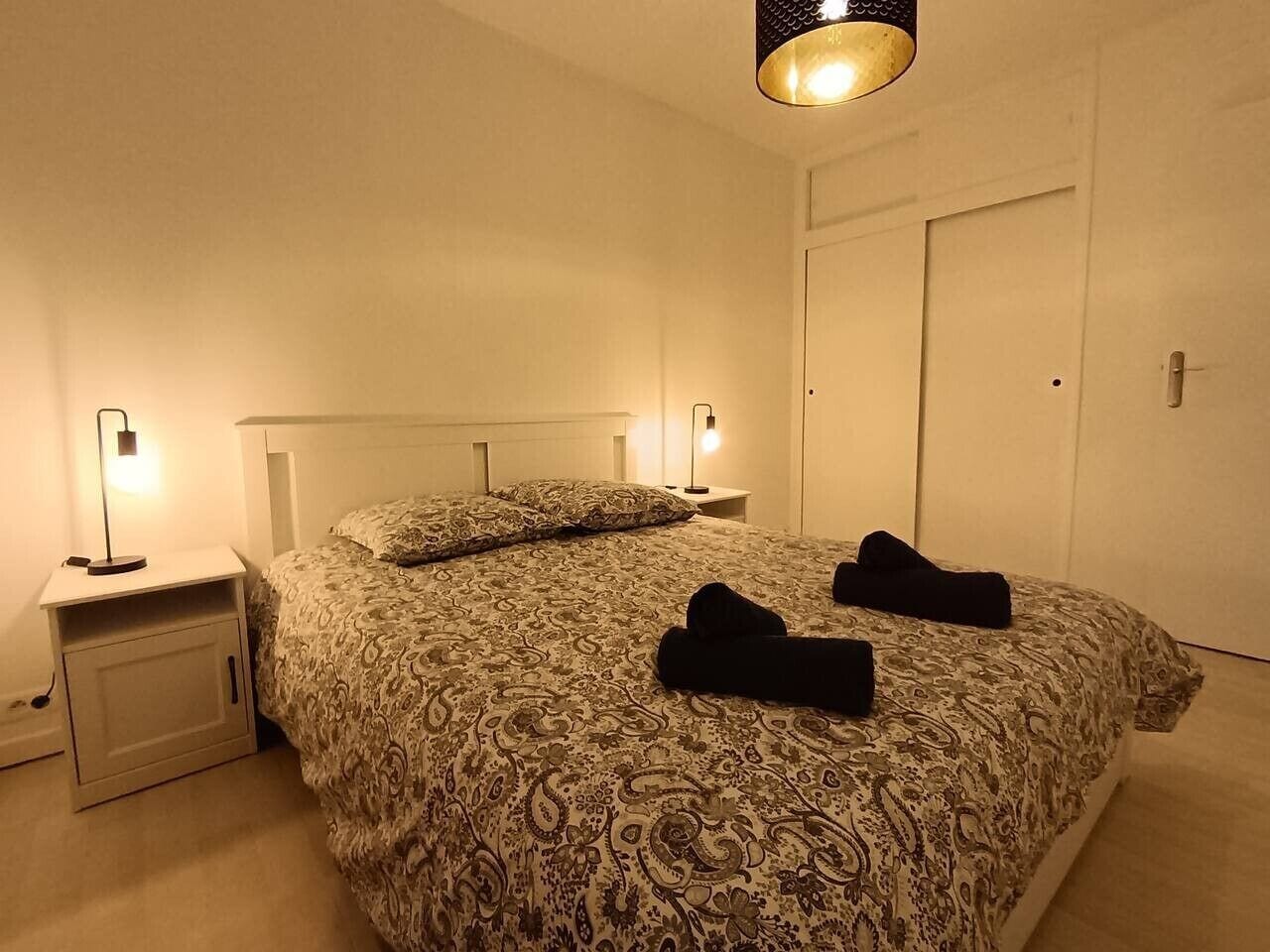 A bedroom with a patterned bedspread, two bedside lamps, a nightstand, and a closed door.