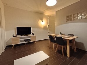 Moderni olohuone, jossa on litteänäyttöinen televisio, puinen ruokapöytä ja tuolit.