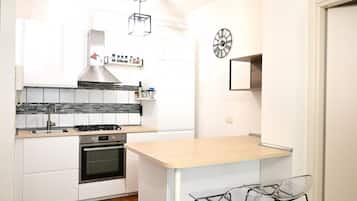 Eine moderne Küche mit weißen Schränken, einer Holz Arbeitsplatte, einem Gasherd, einem Backofen und einer kleinen Kochinsel mit Stühlen.